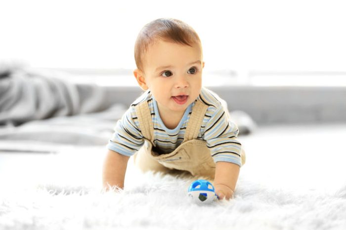 Little baby boy with a toy crawling on the floor at home