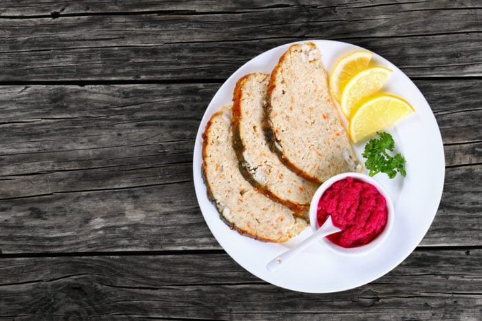 Jewish whitefish or minced-fish forcemeat stuffed inside the fish skin, cut in slices and served with lemon slices and horseradish flavored with beetroot, authentic recipe, view from above