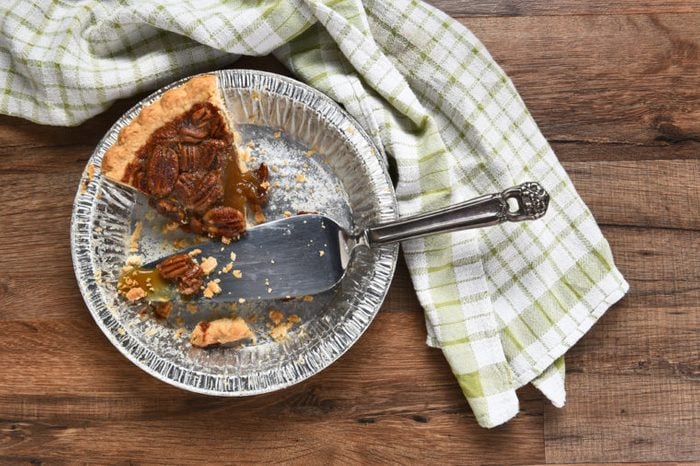 The last slice of a Thanksgiving holiday pecan pie. A tin with spatula on a wood table with kitchen towel. 