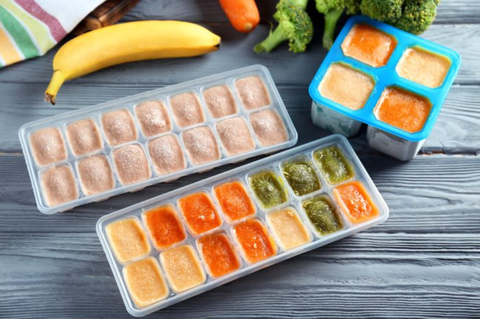 Ice trays with frozen vegetable and fruit puree on wooden table