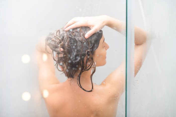 Young woman washing hair with shanpoo in the shower. Back view