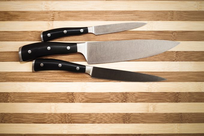 three kitchen knives over bamboo cutting board , 20 cm chef's knife, 16 cm carving knife and 12 cm utility knife