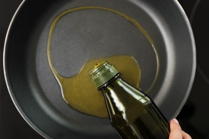 Woman pouring olive oil onto frying pan on stove