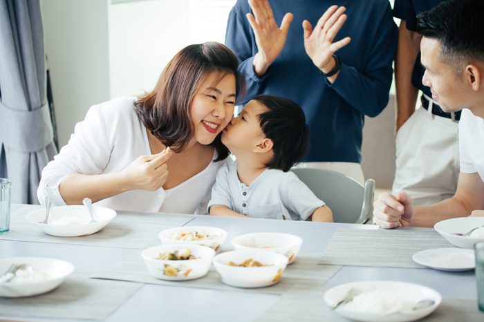 Boy kissing mother on cheeks with the whole Asian family of three generations together at home