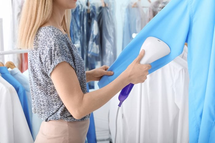 Young woman steaming shirt at dry-cleaner's
