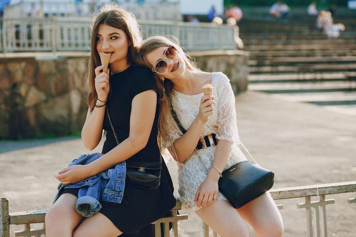 two beautiful young girls sitting in the summer park and eating ice cream