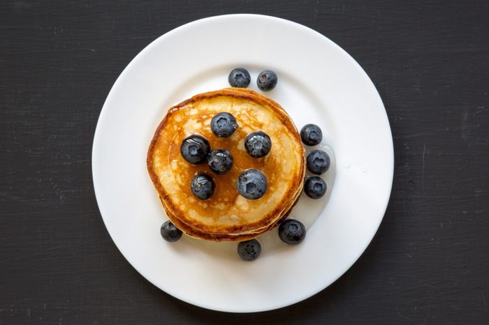 Pancakes with blueberries and honey on white plate on dark wooden background, top view. Flat lay, overhead, from above.
