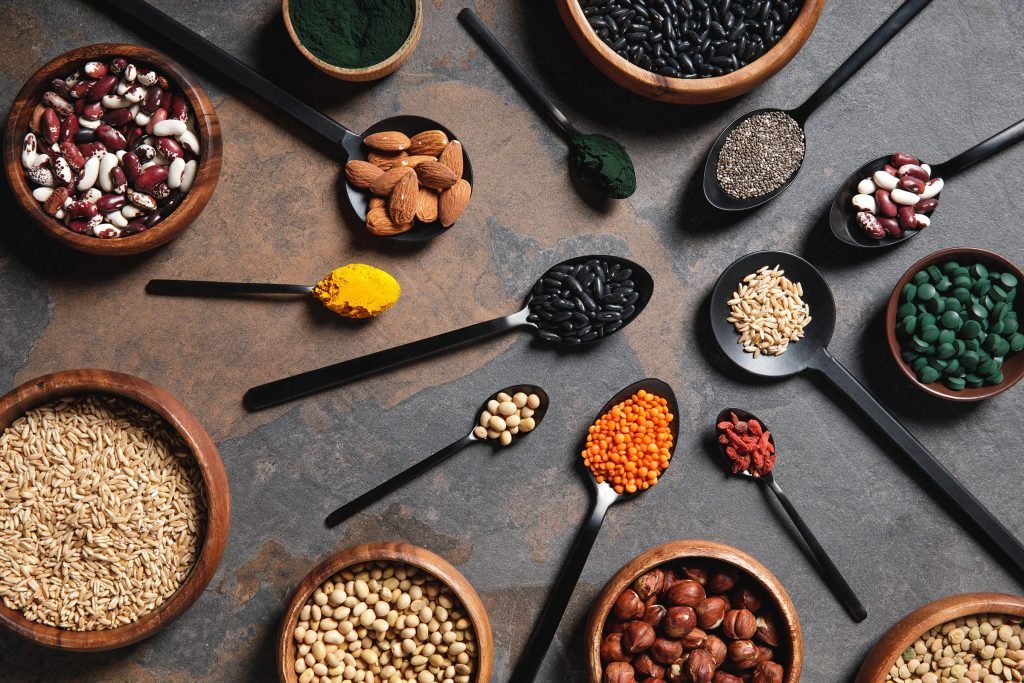 top view of wooden bowls and spoons with superfoods, legumes and grains on table