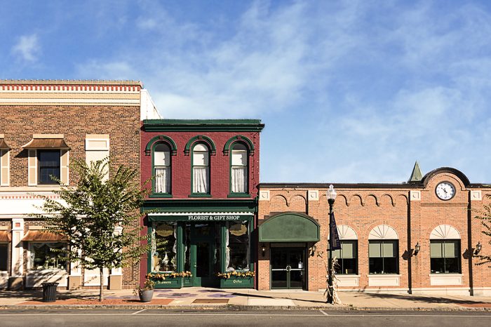A photo of a typical small town main street in the United States of America. Features old brick buildings with specialty shops and restaurants. Decorated with autumn decor. 