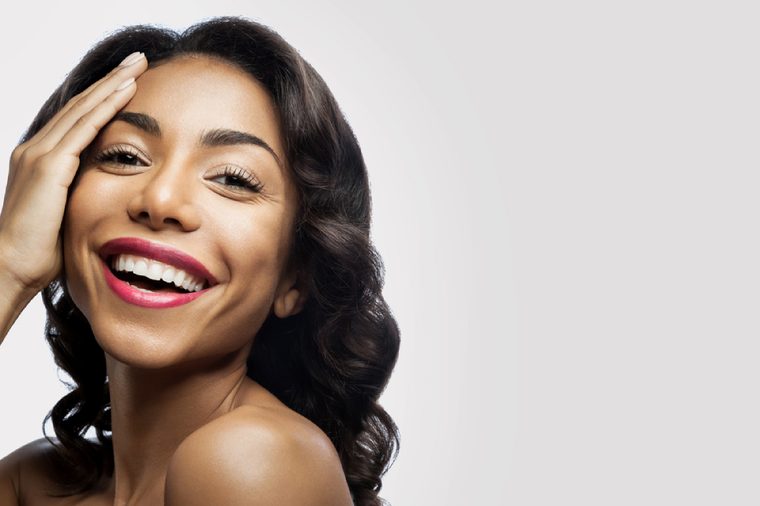 Smiling black girl with perfect healthy skin and makeup. As for the hand of his face on a gray background