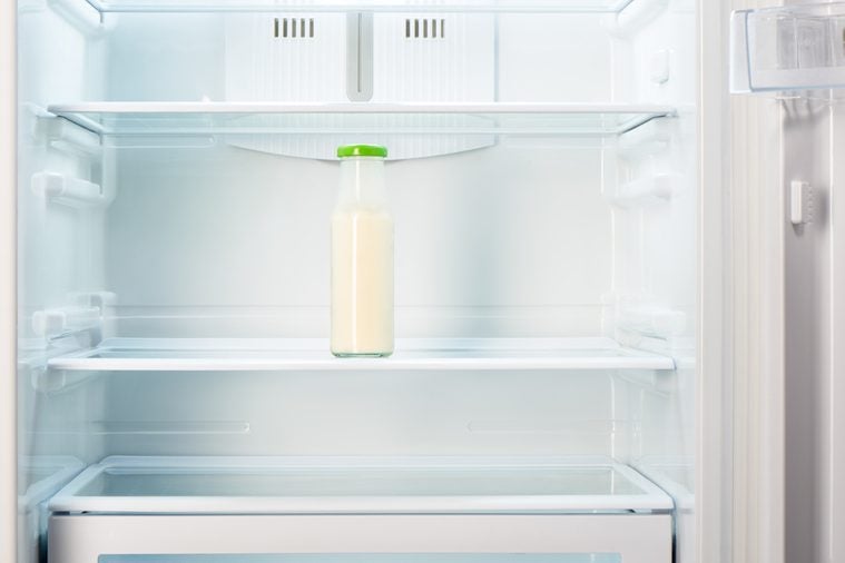 Glass bottle of yogurt on shelf of open empty refrigerator. Weight loss diet concept.
