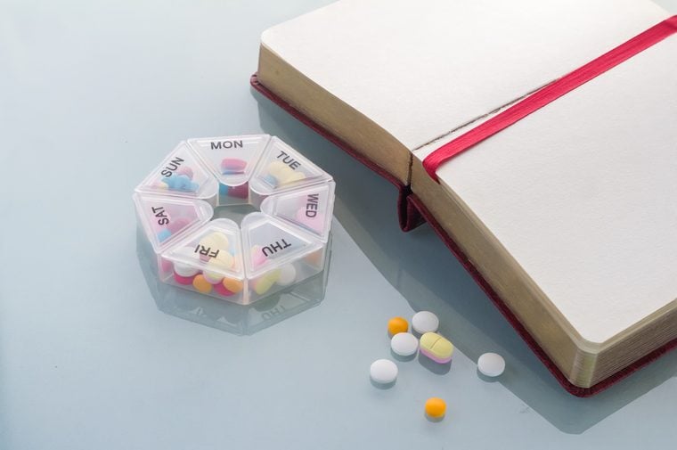 Pills planner with weekly medication capsules in it with notebook on glass top table