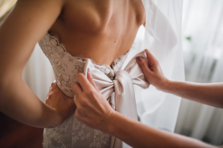 bridesmaid makes bow-knot on the back of brides wedding dress