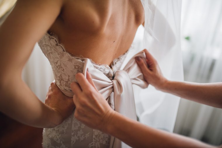 bridesmaid makes bow-knot on the back of brides wedding dress