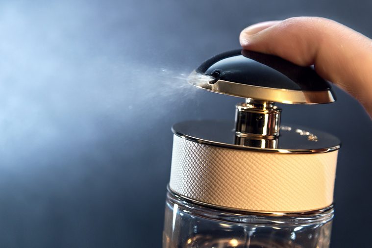 Close up of spraying perfume bottle on a dark grey background.