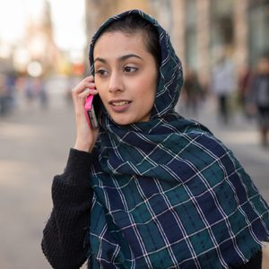 Young woman wearing hijab head scarf in city talking on cell phone