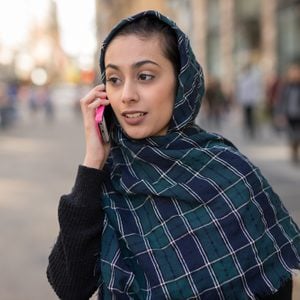 Young woman wearing hijab head scarf in city talking on cell phone