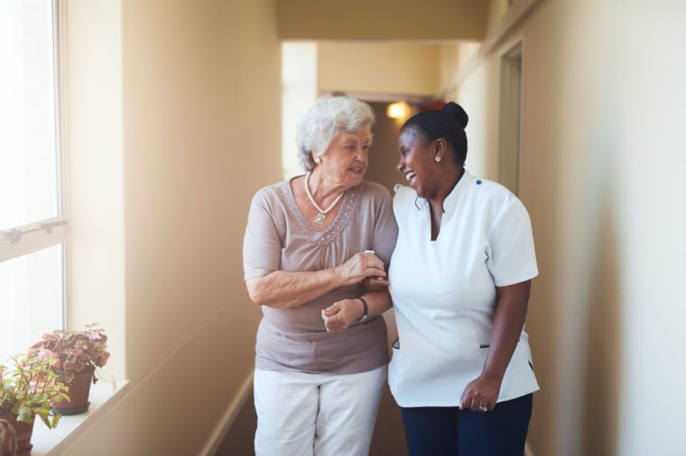 Portrait of happy female caregiver and senior woman walking together at home. Professional caregiver taking care of elderly woman.
