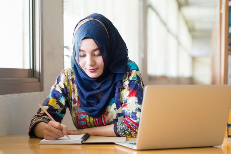 Muslim female working with computer in the room , writing paper.