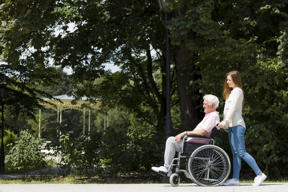 Senior man on a wheelchair going on a walk in the park with a young caregiver