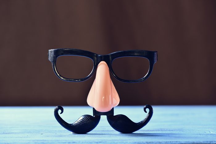 closeup of a fake mustache, nose and eyeglasses on a rustic blue wooden surface