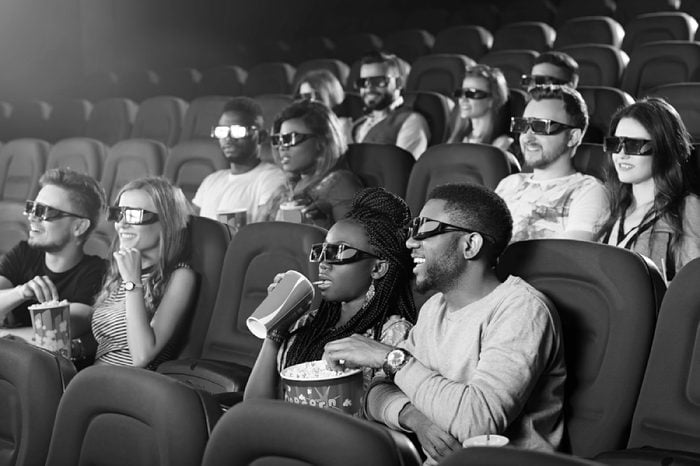 Entertainment snack. Young African man eating popcorn while watching a 3D movie his girlfriend sipping her drink at the cinema