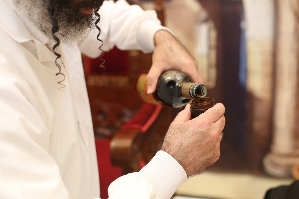 Rabbi holds kiddish cup with wine in front of Groom and Bride