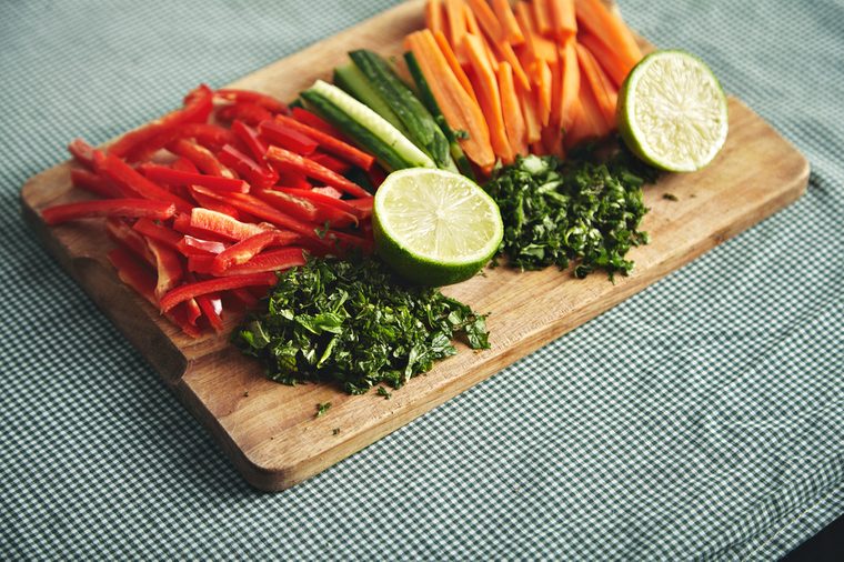 Colorful salad ingredients on a wooden cutting board on a table covered with checkered tablecloth