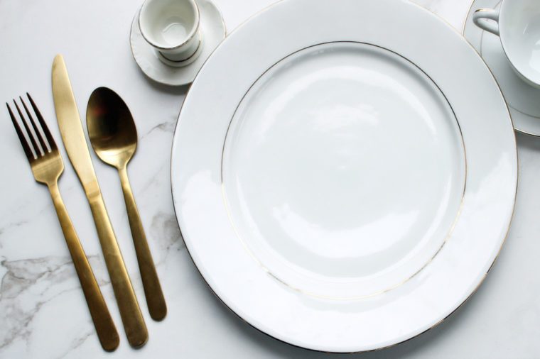 Over head flat lay view of white and gold fine china place setting. Gold silverware and elegant china.