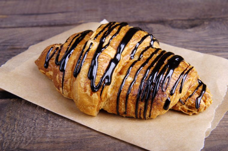 Croissant with chocolate topping on a dark wooden background.