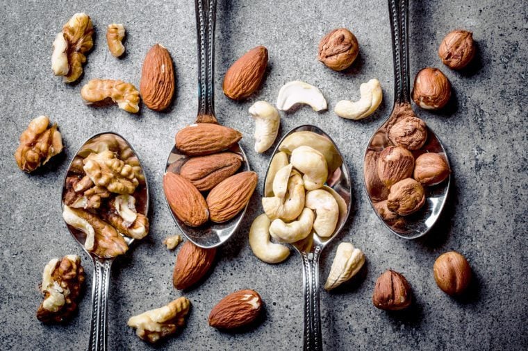 Walnuts, hazelnuts, almonds and cashew on metal silver spoons.