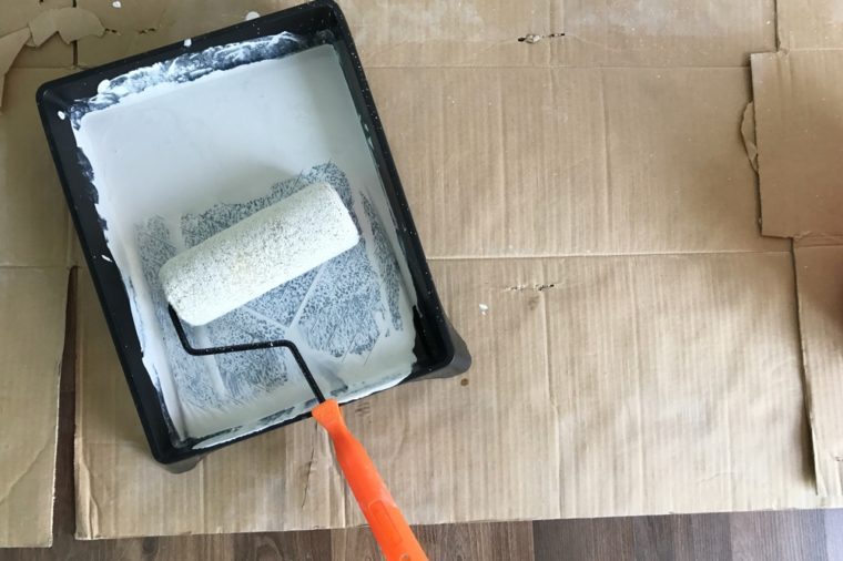 Paint roller in paint tray with white color in the tray on brown paper on wooden floor