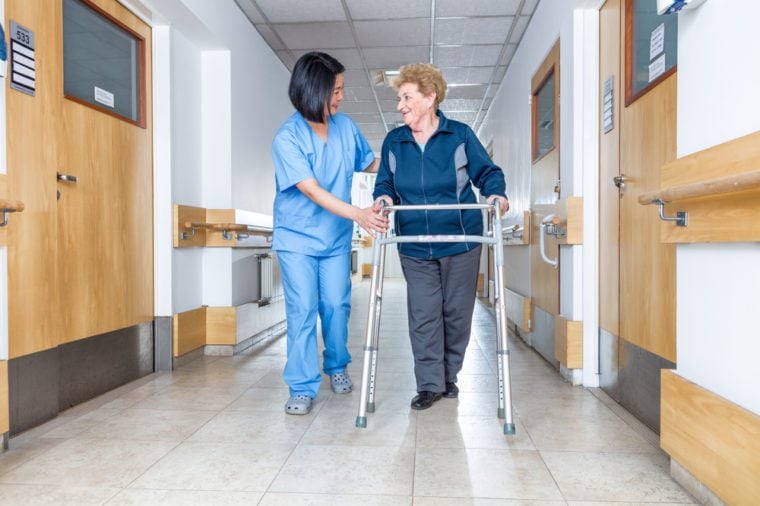 Senior female patient being assisted by female asian nurse in using walker.