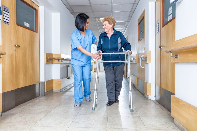 Senior female patient being assisted by female asian nurse in using walker.
