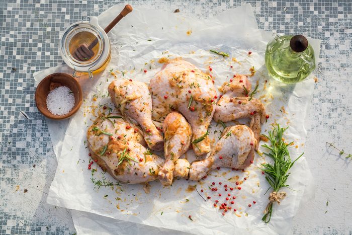Seasoning chicken legs with rosemary on an old table