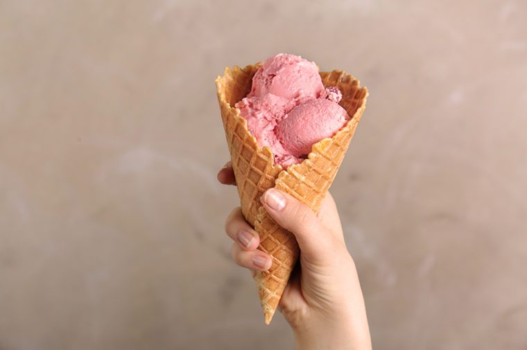 Female hand holding waffle cone with tasty ice cream on light background