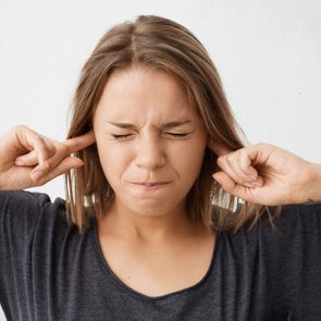 Close up portrait of angry stressed out young woman plugging ears with fingers and closing eyes tight, irritated with loud annoying noise, having headache or migraine. Negative human emotions