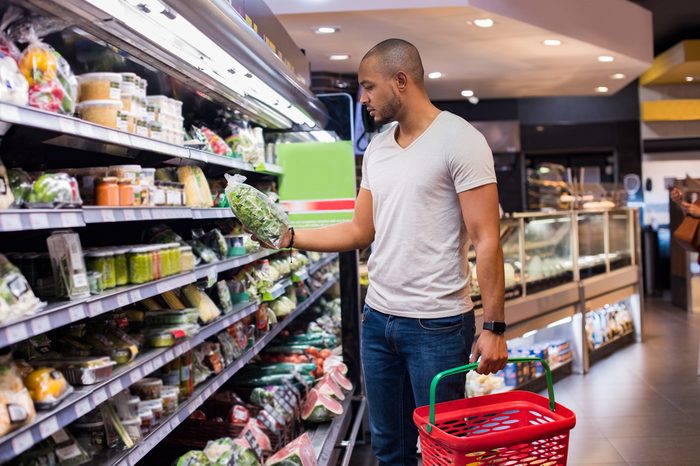 Young african man buying vegetables in grocery section at supermarket. Black man choose vegetables in the supermarket while holding grocery basket. Man shopping veggies at supermarket.