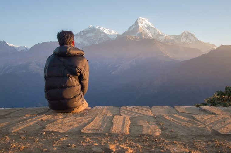 A young man sit on the floor is looking to the high mountains in the Himalaya, Nepal