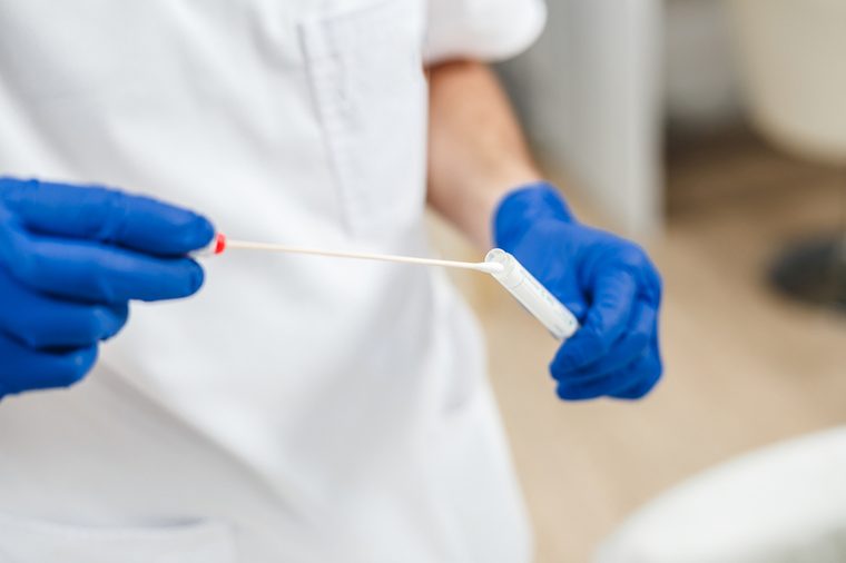 Closeup DNA test tube and cotton swab, wipe test in man hands. Men's hands in blue gloves.