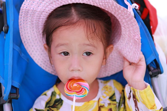 Close-up Beautiful cute little girl wear straw hat eating lollipop