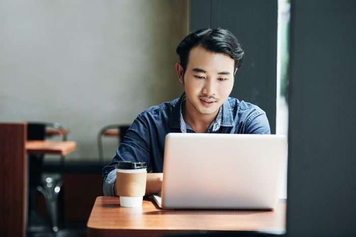 Young Asian man sitting in coffeeshop table and working on laptop