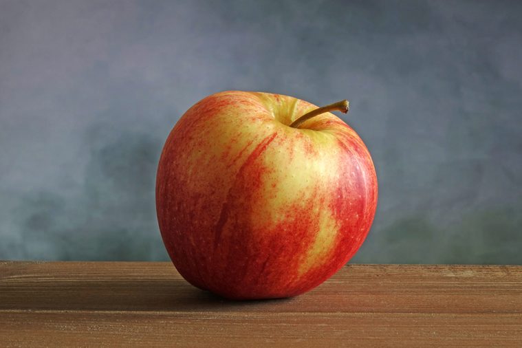 Organic Gala apple on wood table. Selective focus, blurred concrete wall background.