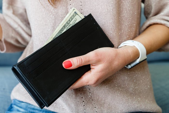 female hand close-up hold a black purse in which dollars lie