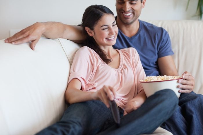 Delighted couple watching TV while eating popcorn in their living room