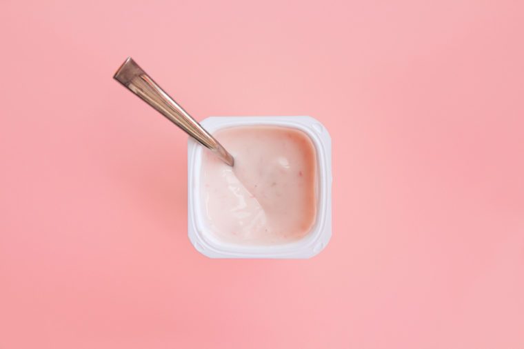 Delicious strawberry yogurt or pudding in white plastic cup on pink background with copy space. Strawberry pink yoghurt with spoon in it. Minimal style. Flat lay, top view.