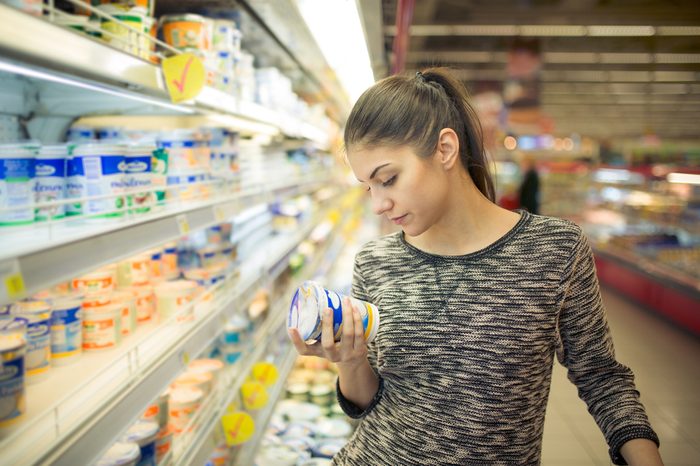 Young woman reading ingredients,declaration or expiration date on a dairy product before buying it.Curious woman reading nutritional values of the food.Shopping in the supermarket grocery store.