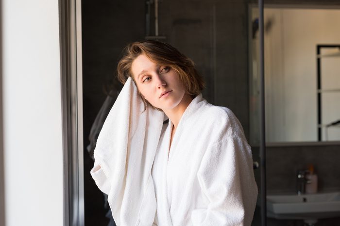 pensive young woman in bathrobe drying hair with towel in bathroom