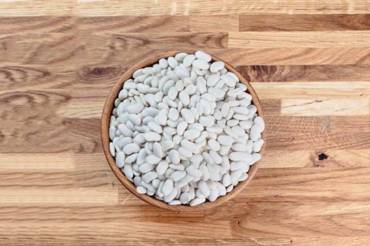 Beans white in a wooden bowl standing on the kitchen table made of oak. Top view.