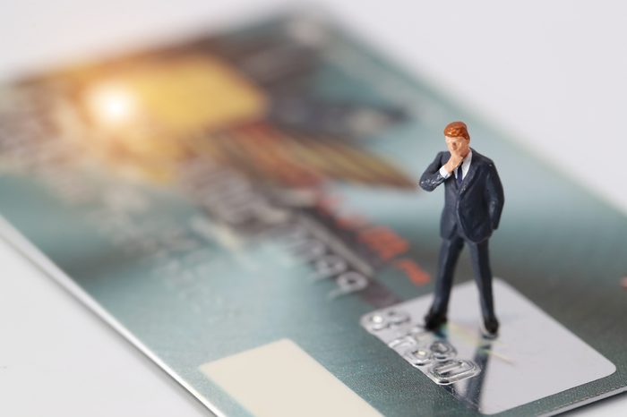 Miniature people: businessman standing and thinking of something on credit card as payment and purchase online solution (e-commerce and shopping concept)